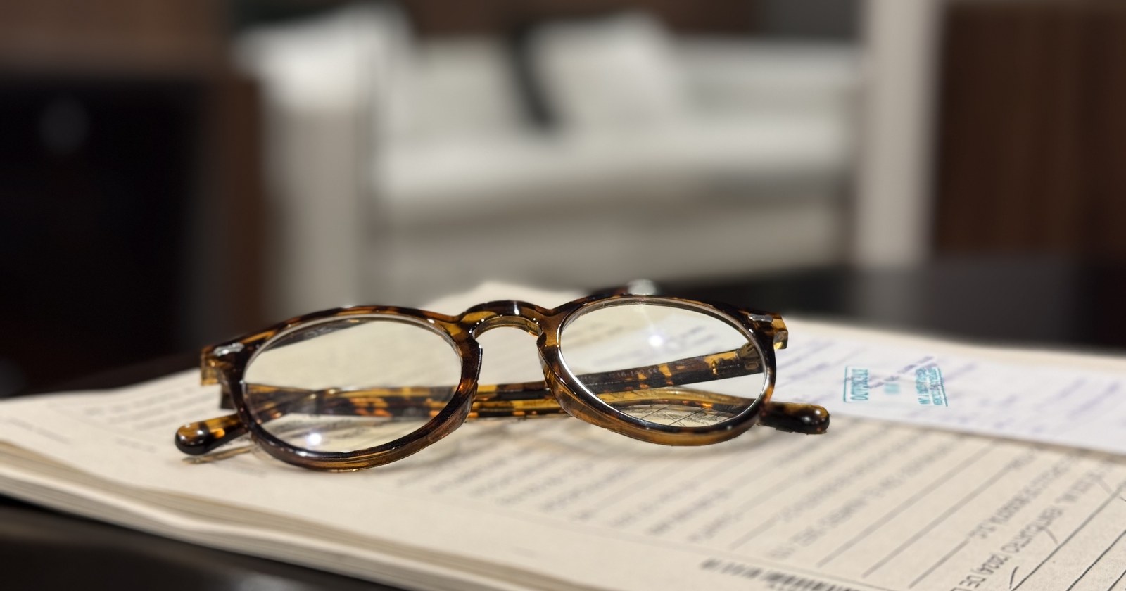 Gafas de lectura apoyadas sobre un legajo de documentos procesales en un escritorio
